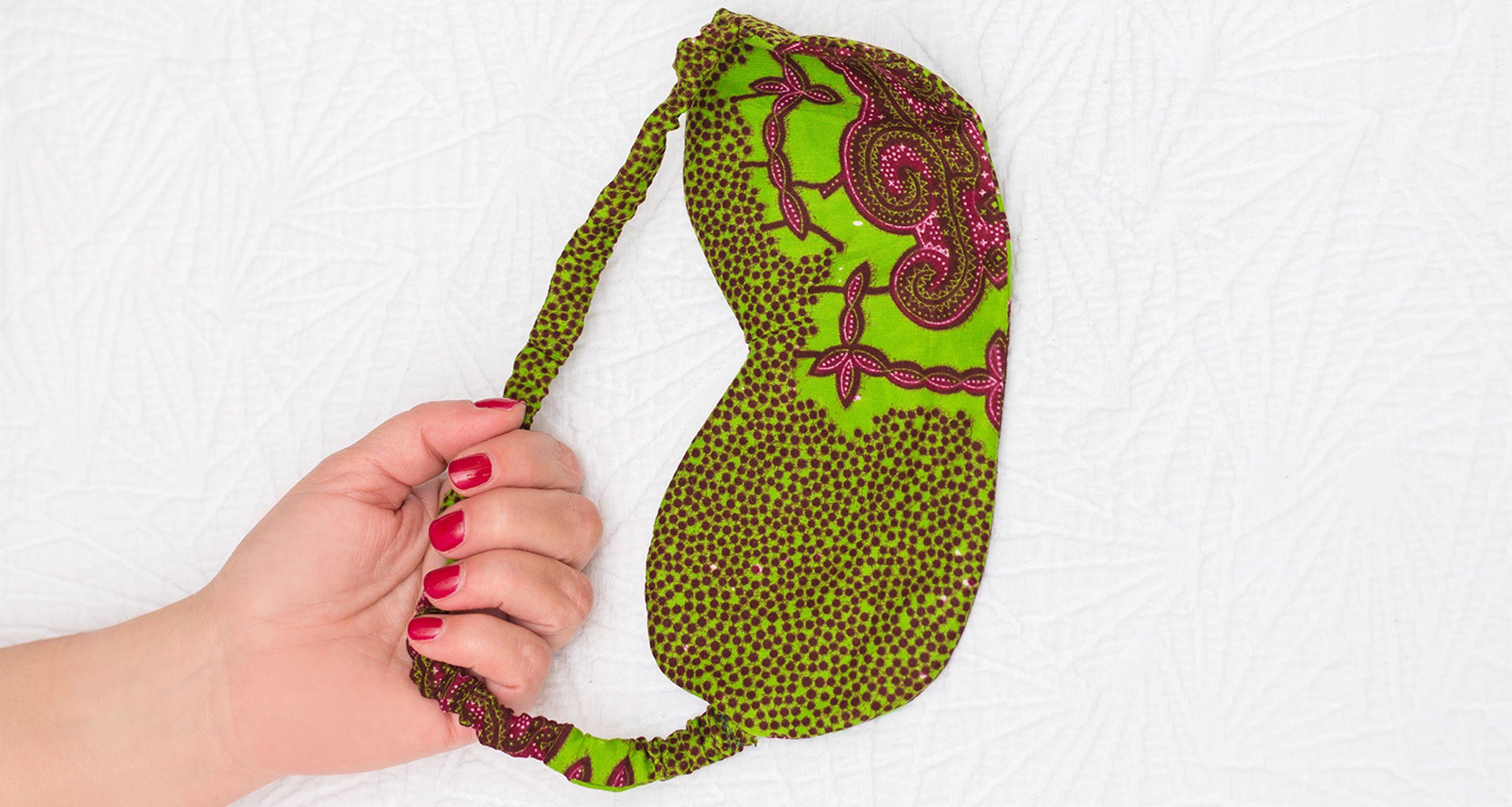 A hand holding a green and pink patterned bag.