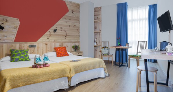 Habitación de hotel con dos camas, un escritorio, una silla, un televisor y una ventana con cortinas.