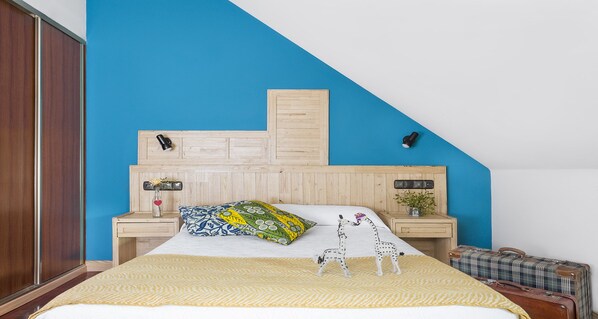 A bedroom with a bed, wooden headboard, bedside tables, and a suitcase. - Hotel San Miguel Gijón (Gijon)