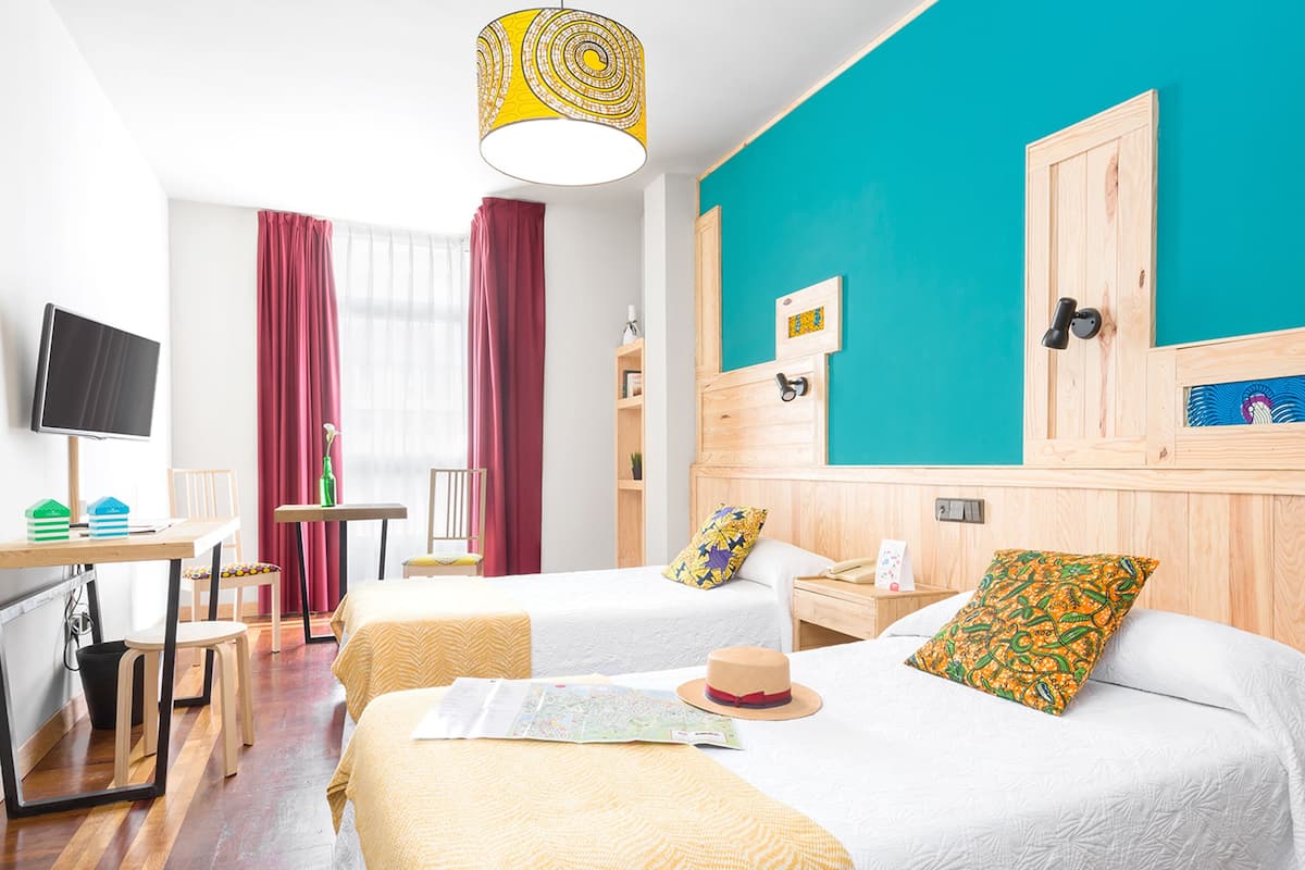 Quarto de hotel com duas camas, uma escrivaninha, uma cadeira, uma televisão e uma janela com cortinas.