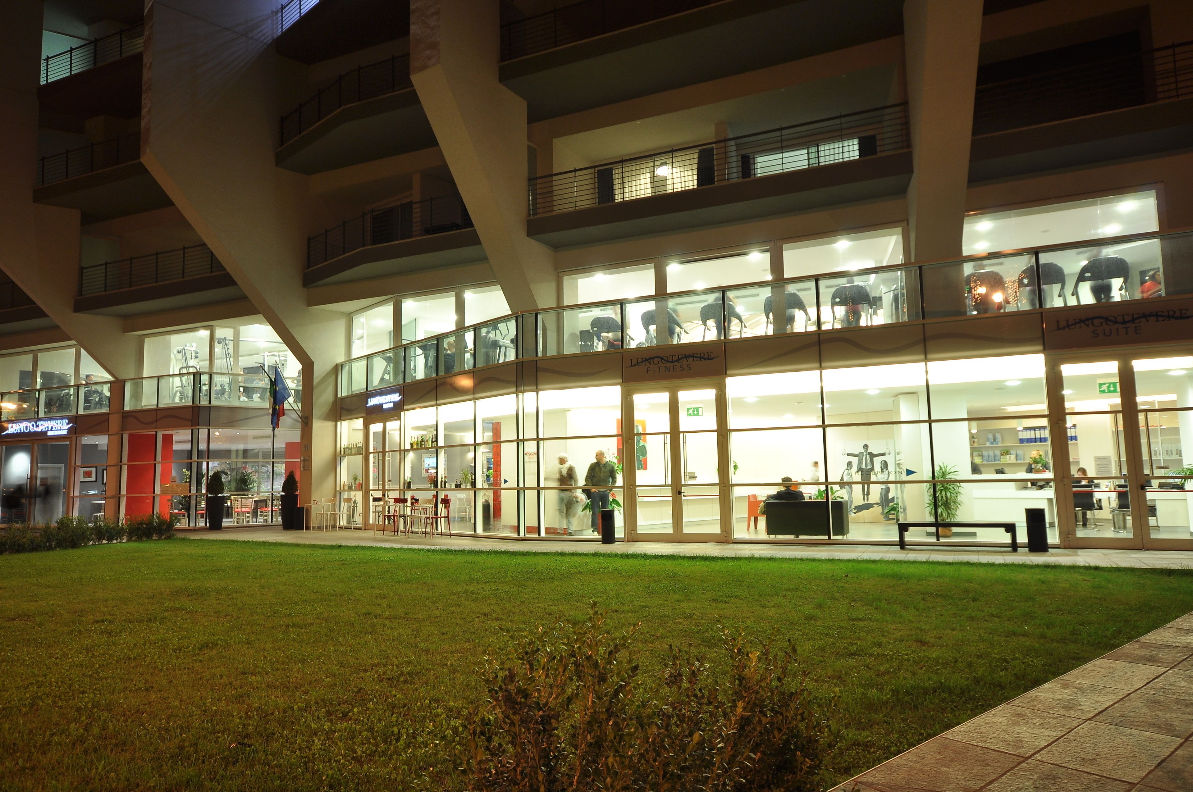 A hotel with a modern glass facade, outdoor seating area, and a visible entrance.