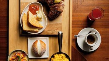 Ein Holztablett mit Croissants, Toast, Rührei und einer Schüssel Obstsalat.