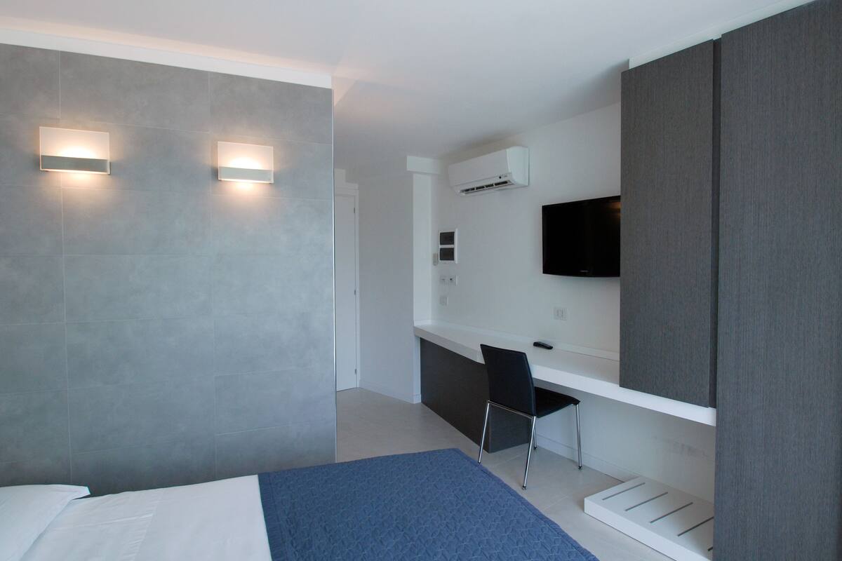 Ein modernes Hotelzimmer mit Bett, Schreibtisch, Stuhl und einem an der Wand befestigten Fernseher.