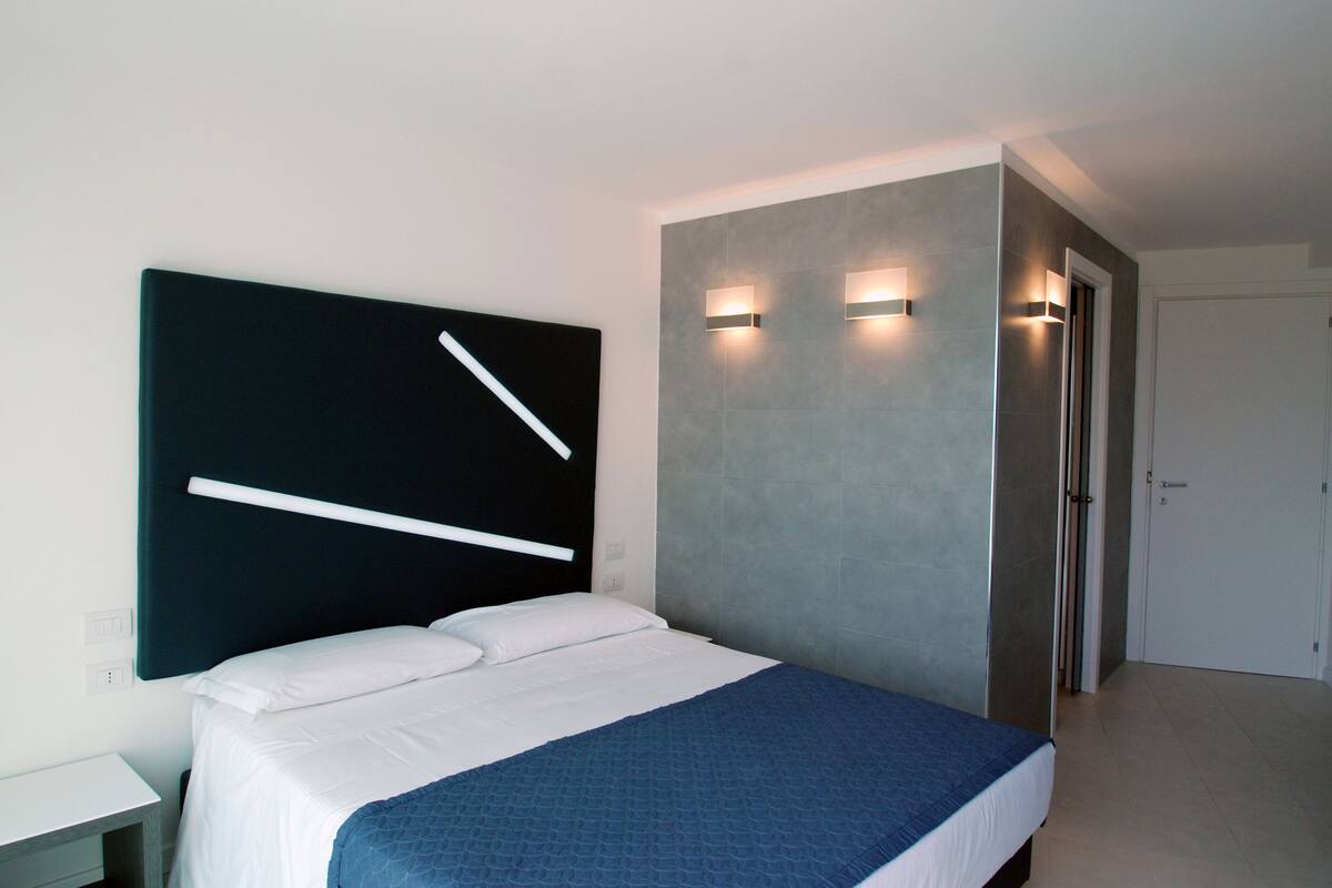 Ein modernes Hotelzimmer mit einem großen Bett, einem Nachttisch und einer Wandleuchte.