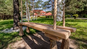 Un banco de madera con soportes de cuerda, rodeado de árboles y un espacio cubierto de césped.