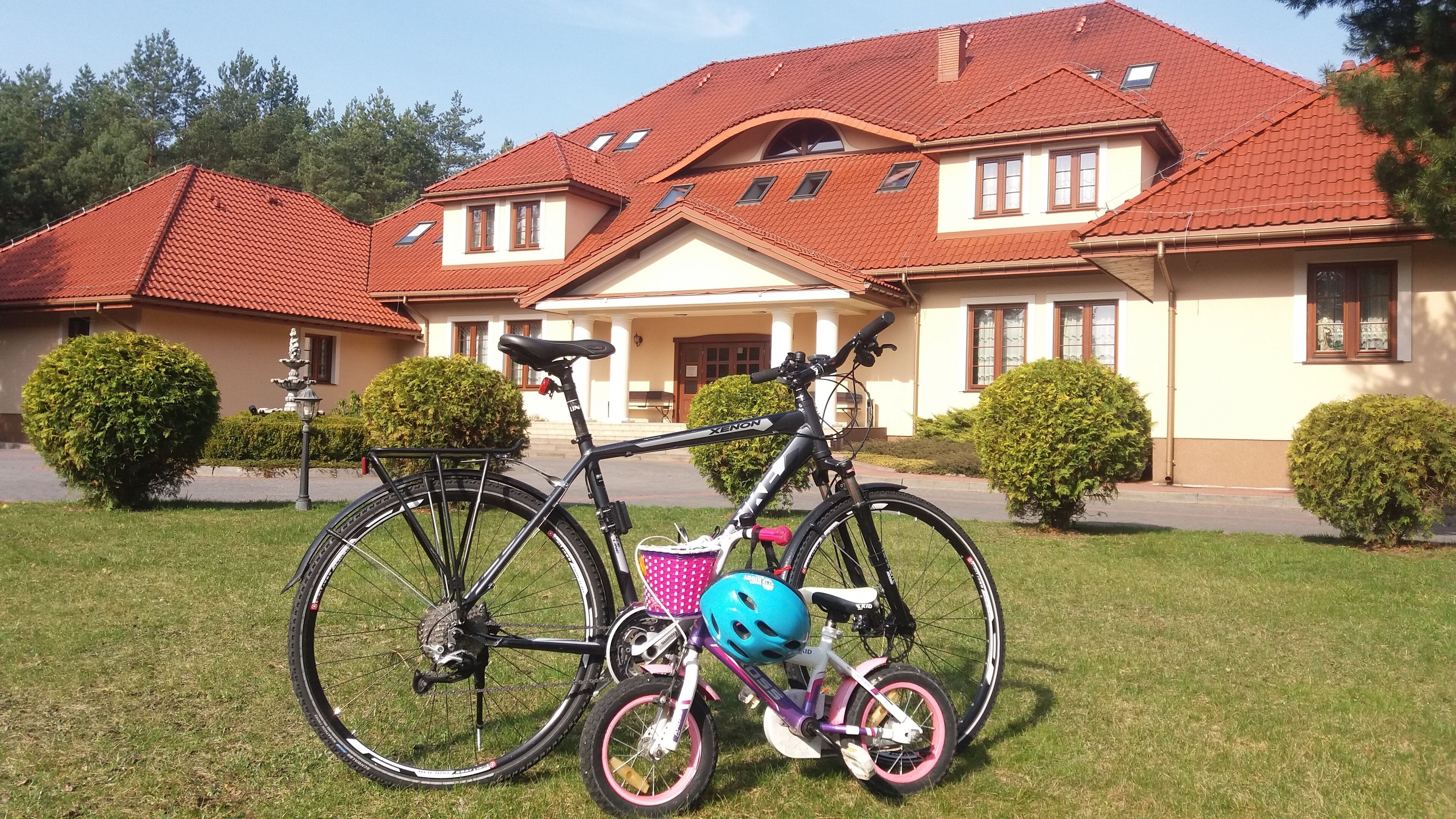 A bicycle with a helmet and a pink basket parked in front of a house with a red roof and white walls.
