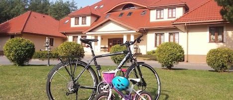 Una bicicleta con casco y una cesta rosa estacionada frente a una casa de techo rojo y paredes blancas.