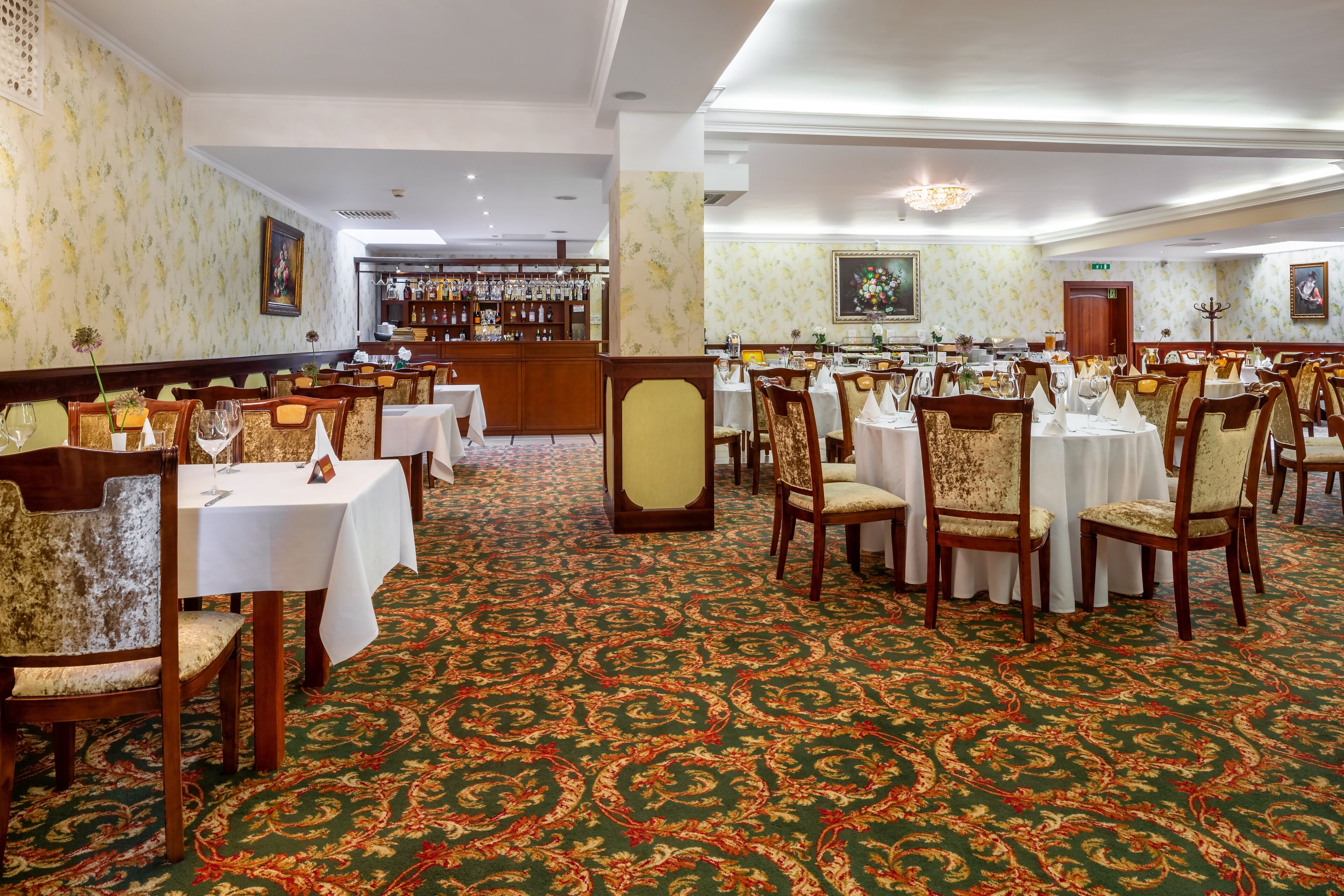 Un'elegante sala da pranzo con diversi tavoli e sedie, un bar sullo sfondo e un tappeto decorato.
