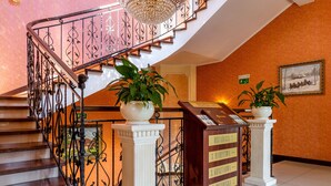 Una imponente escalera con candelabro, plantas en macetas y un mostrador de recepción.