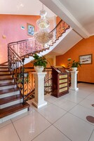 Uma escadaria imponente com um candelabro, plantas em vasos e um balcão de recepção.