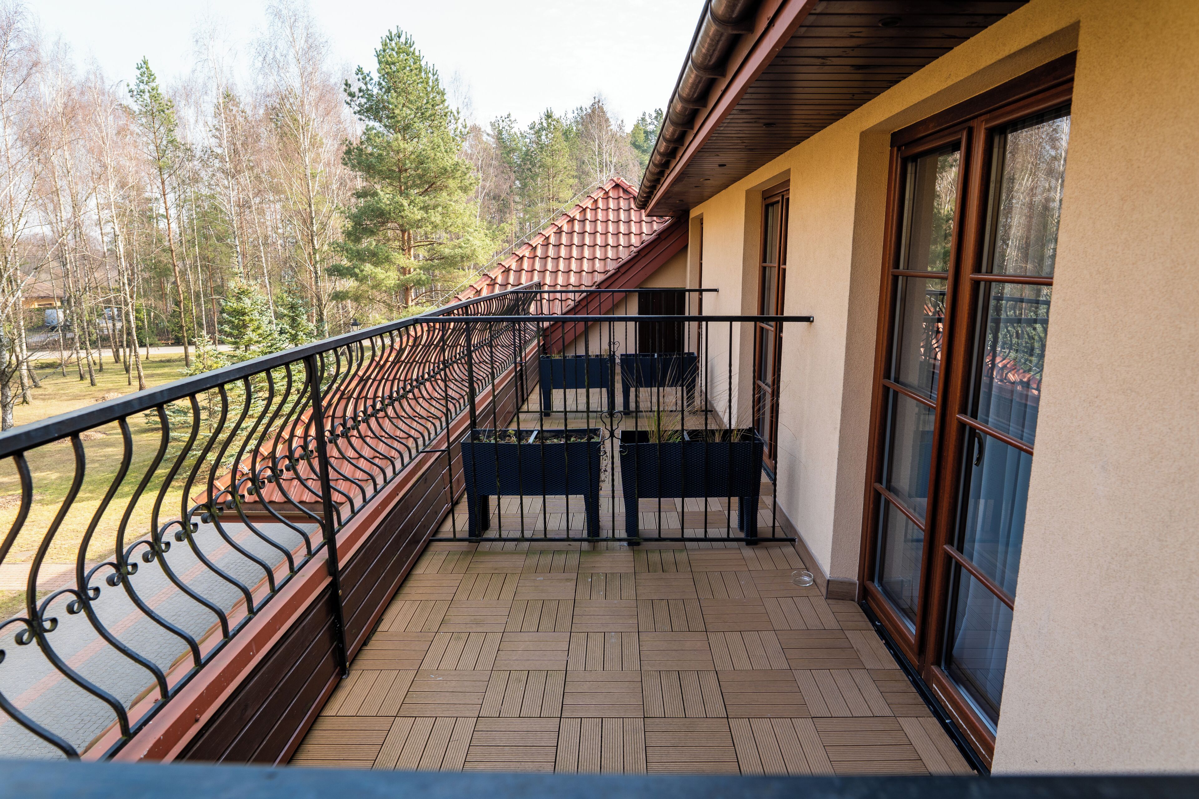 A balcony with a wooden floor, metal railing, and a view of trees.