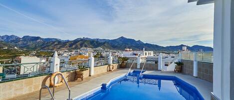 Una piscina en la azotea con vistas a montañas y a un paisaje urbano.