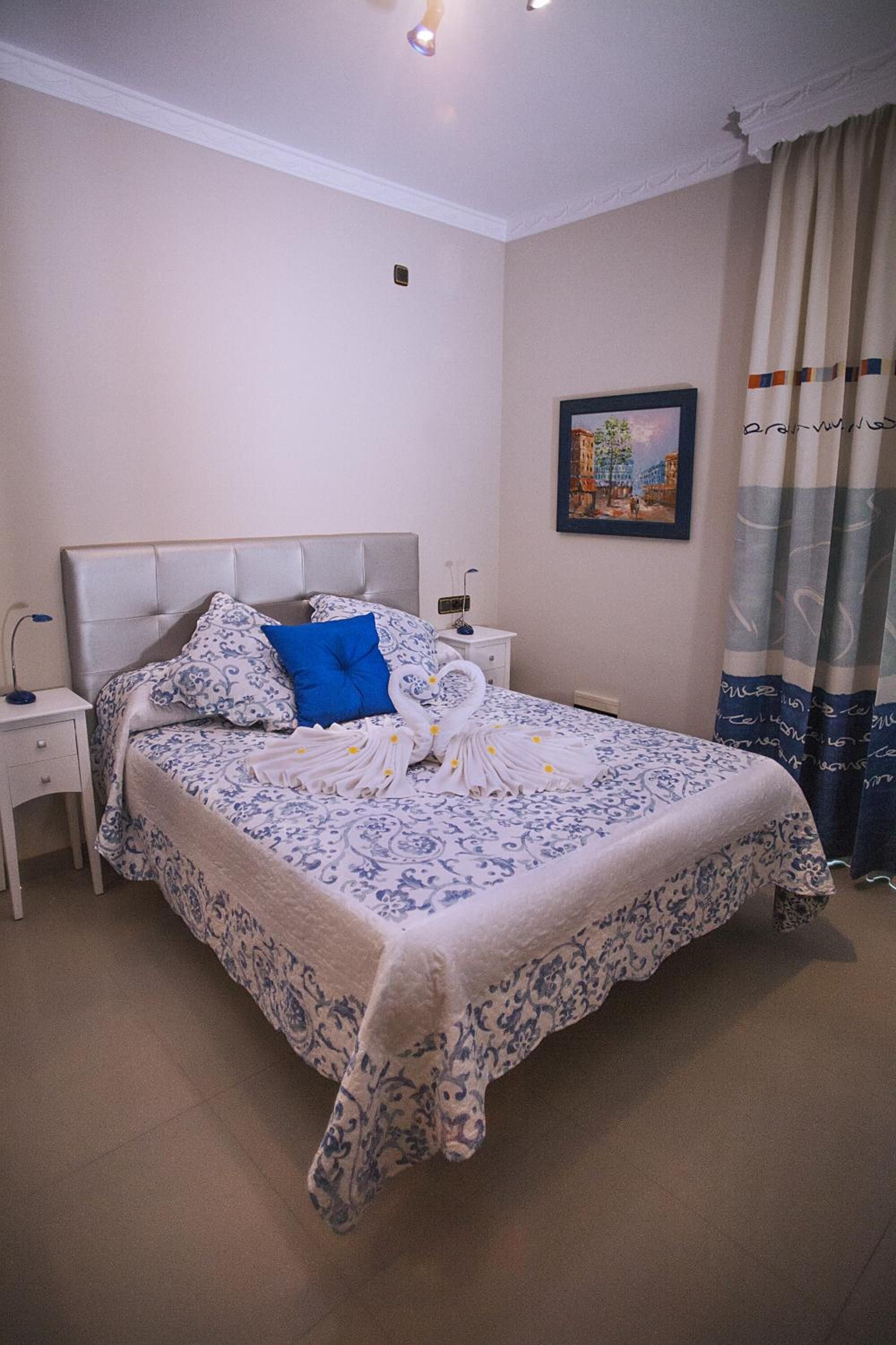 Un lit bien fait, avec une couvre-lit à motifs, un oreiller bleu et une tête de lit blanche.
