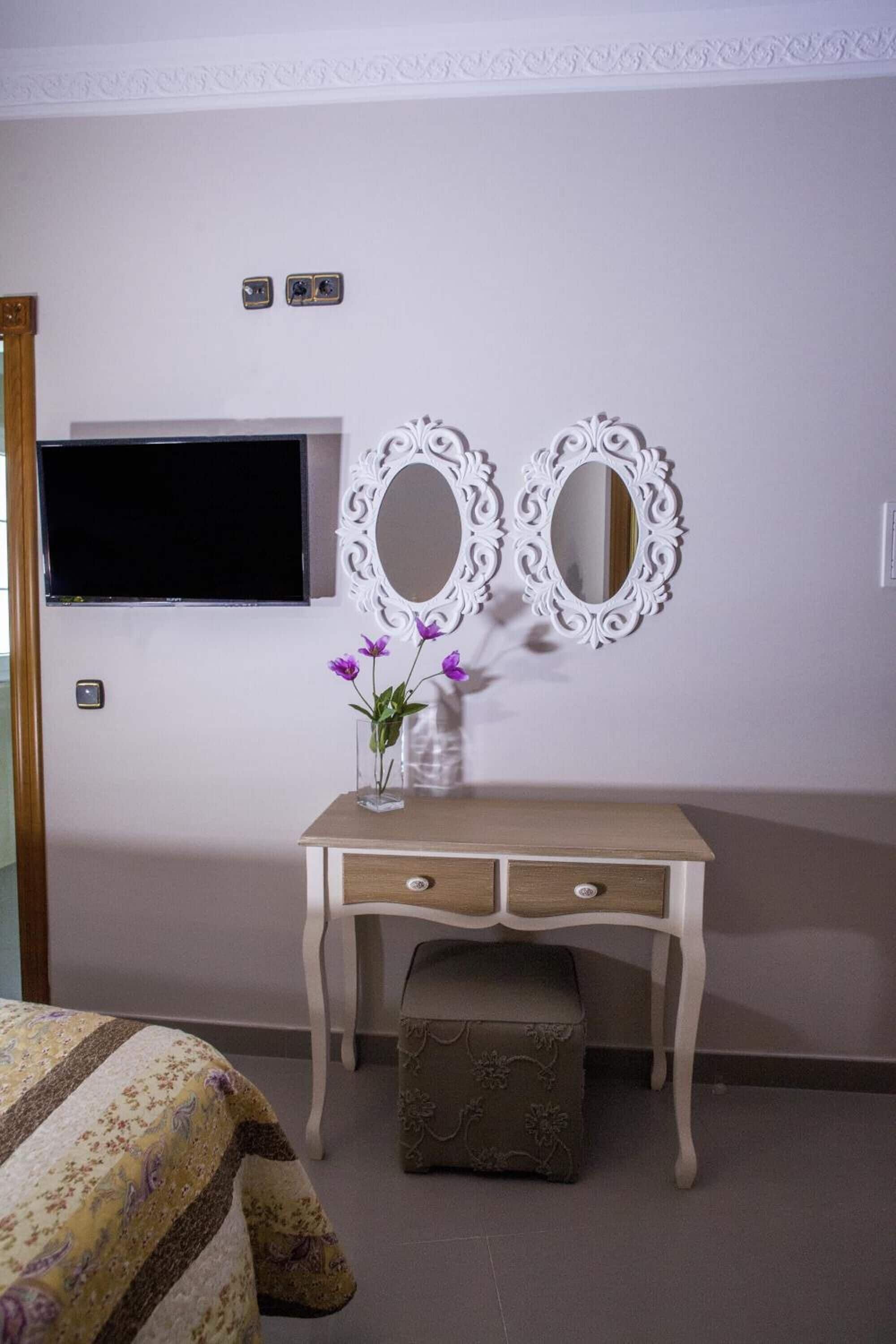 Une chambre à coucher comprenant un lit, une commode, un téléviseur et deux miroirs fixés au mur.