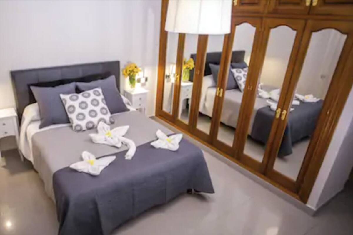 Un dormitorio ordenado con cama, mesitas de noche, un espejo y un armario.