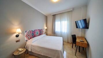 A hotel room with a bed, bedside lamps, a desk with a chair, a television, and a telephone on a side table.