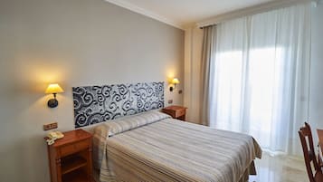 Ein Hotelzimmer mit einem Bett, zwei Nachttischen, einer Lampe, einem Telefon und einem Fenster mit Vorhängen.