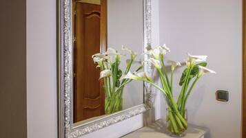 A white console table with a mirror above it, a vase with white flowers, and a wooden door in the background.