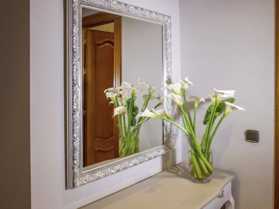 A white console table with a mirror above it, a vase with white flowers, and a wooden door in the background.