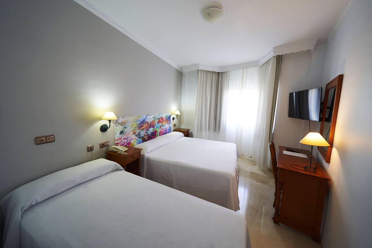 Habitación de hotel con dos camas, un televisor, un escritorio con lámpara y un cuadro en la pared.