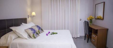 A hotel room with a bed, a desk, a chair, a TV, and a mirror.