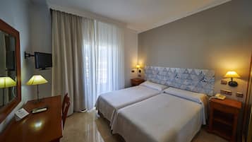 Una habitación de hotel con dos camas, un escritorio con lámpara, televisión y teléfono en una mesita de noche.