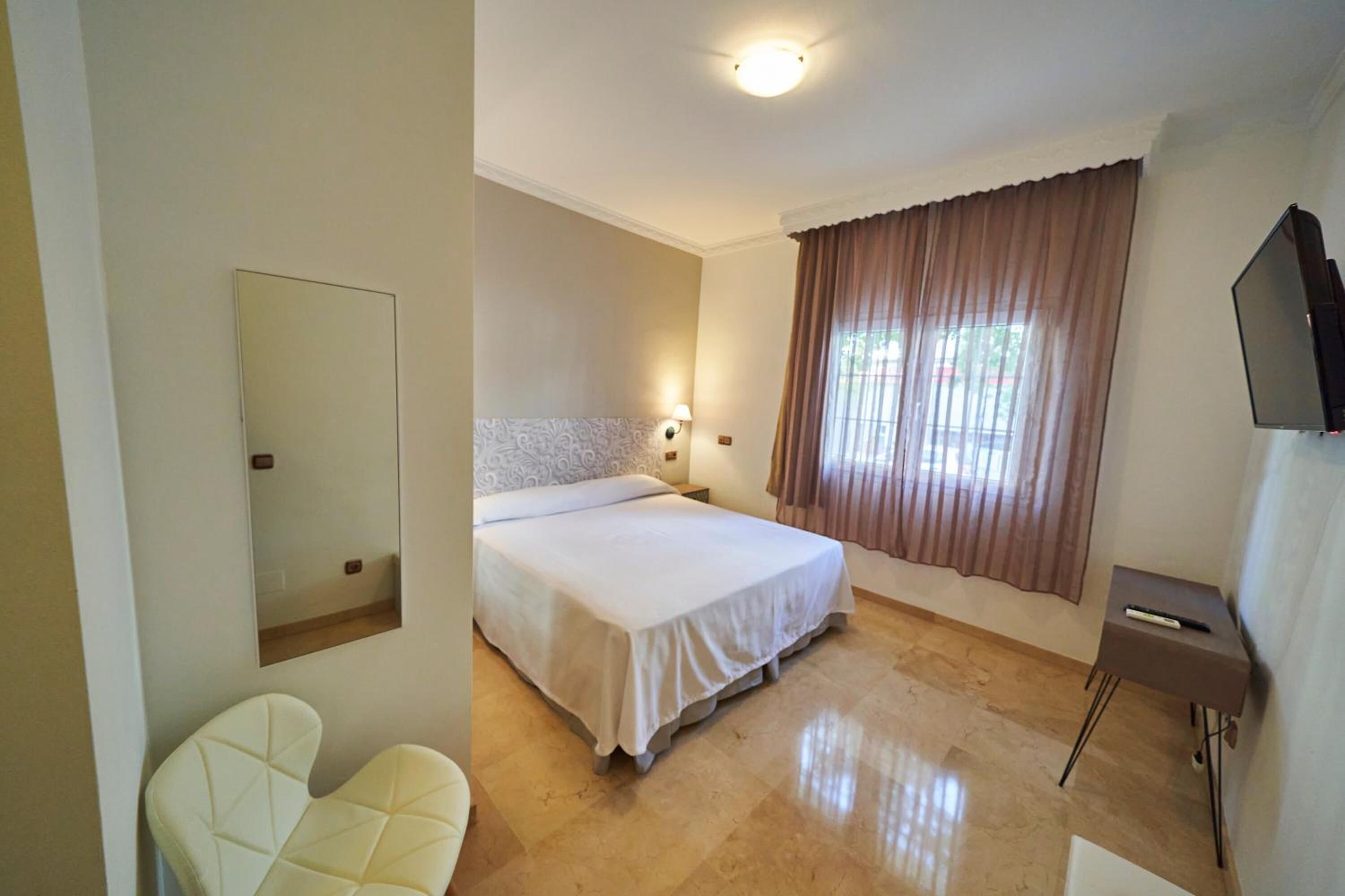 A hotel room with a bed, a chair, a TV, and a window with curtains.