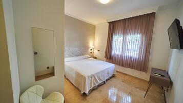 Ein Hotelzimmer mit Bett, Sessel, Fernseher und einem fenster mit Vorhängen.