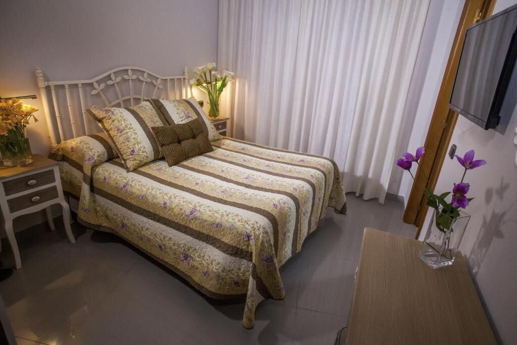 A neatly arranged bedroom with a bed, bedside tables, a TV, and a small desk.