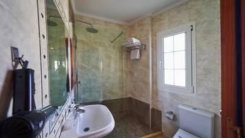 Un baño con ducha de vidrio, lavamanos, inodoro y ventana.
