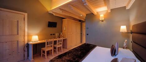 A bedroom with a bed, bedside lamps, a desk with chairs, and wooden cabinets.