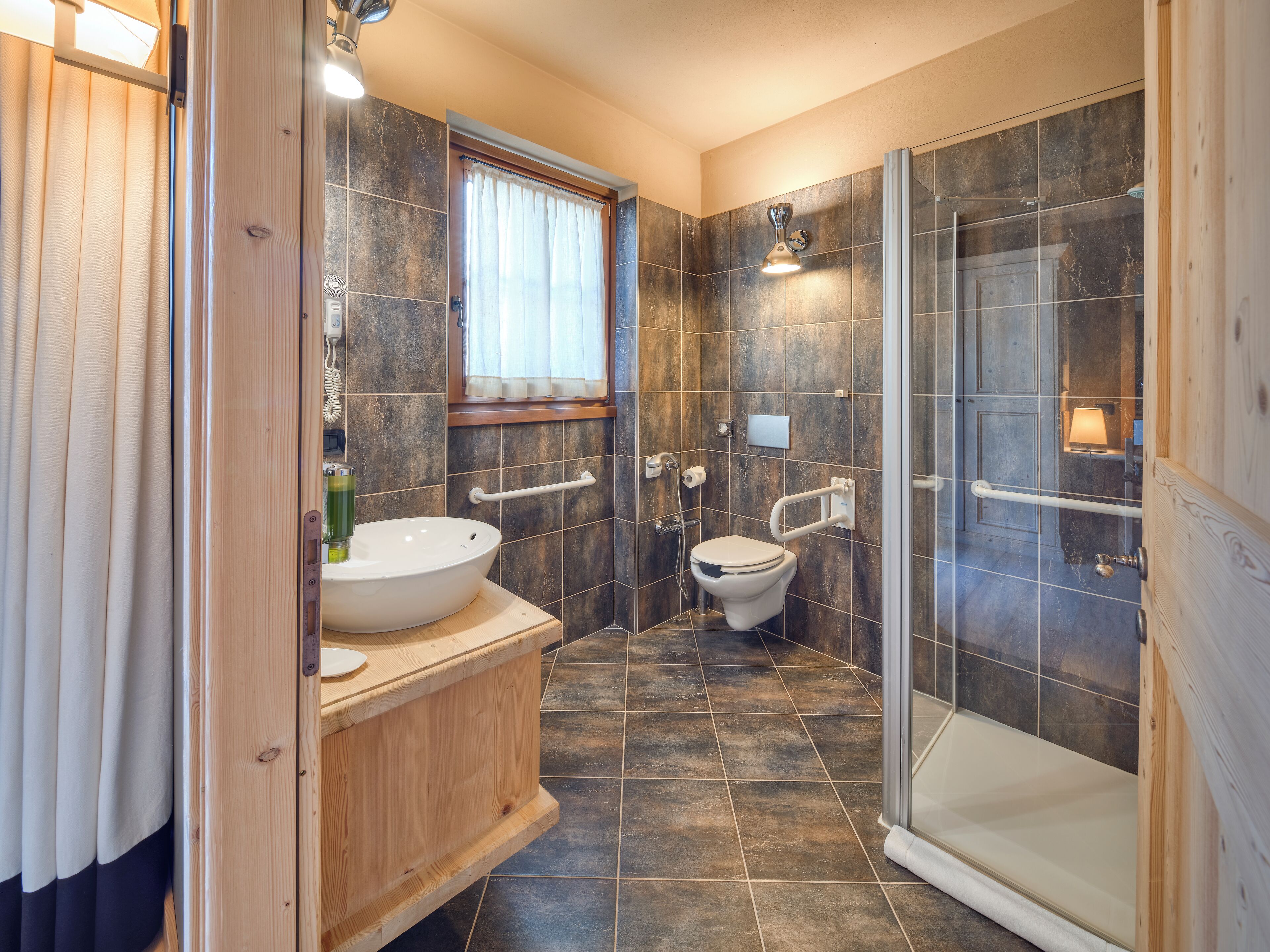 Un baño moderno con tocador de madera, un lavamanos, un inodoro y una zona de ducha con mampara de cristal.