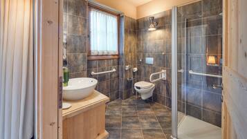 Un baño moderno con tocador de madera, un lavamanos, un inodoro y una zona de ducha con mampara de cristal.