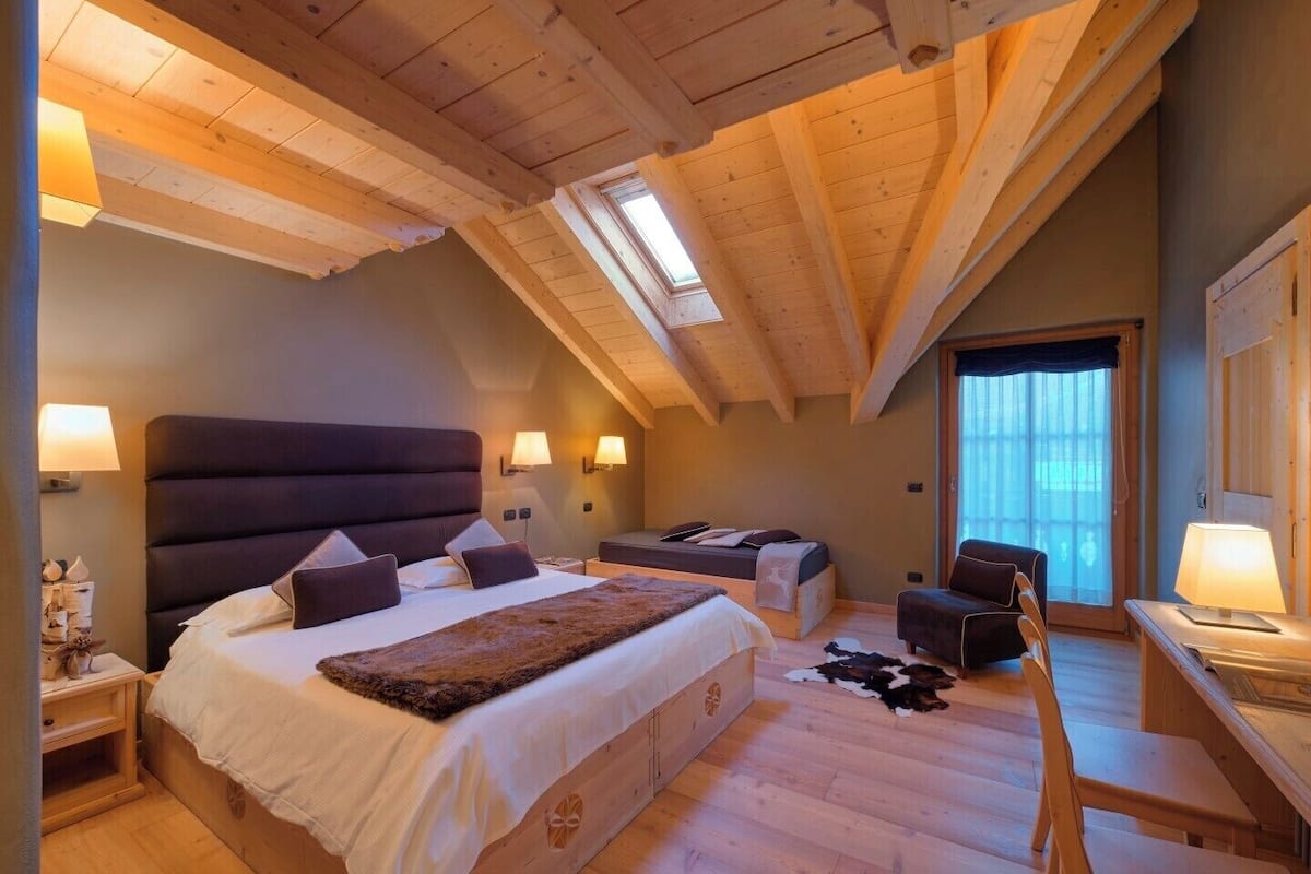 A bedroom with a large bed, a desk, and a chair. There is a skylight and a window.