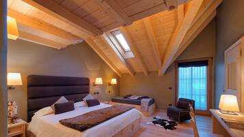 Une chambre avec un grand lit, un bureau et une chaise. Elle est dotée d’une lucarne et d’une fenêtre.