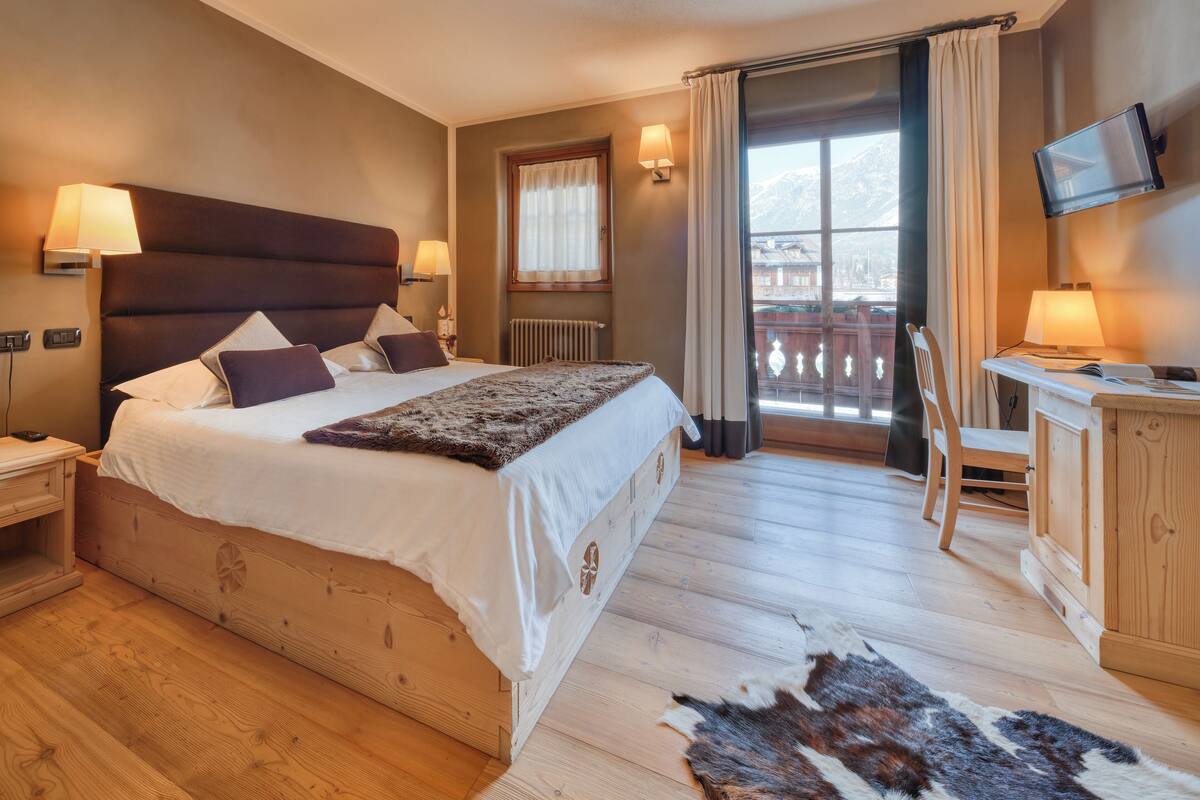 A bedroom with a large bed, a desk, a chair, and a TV.