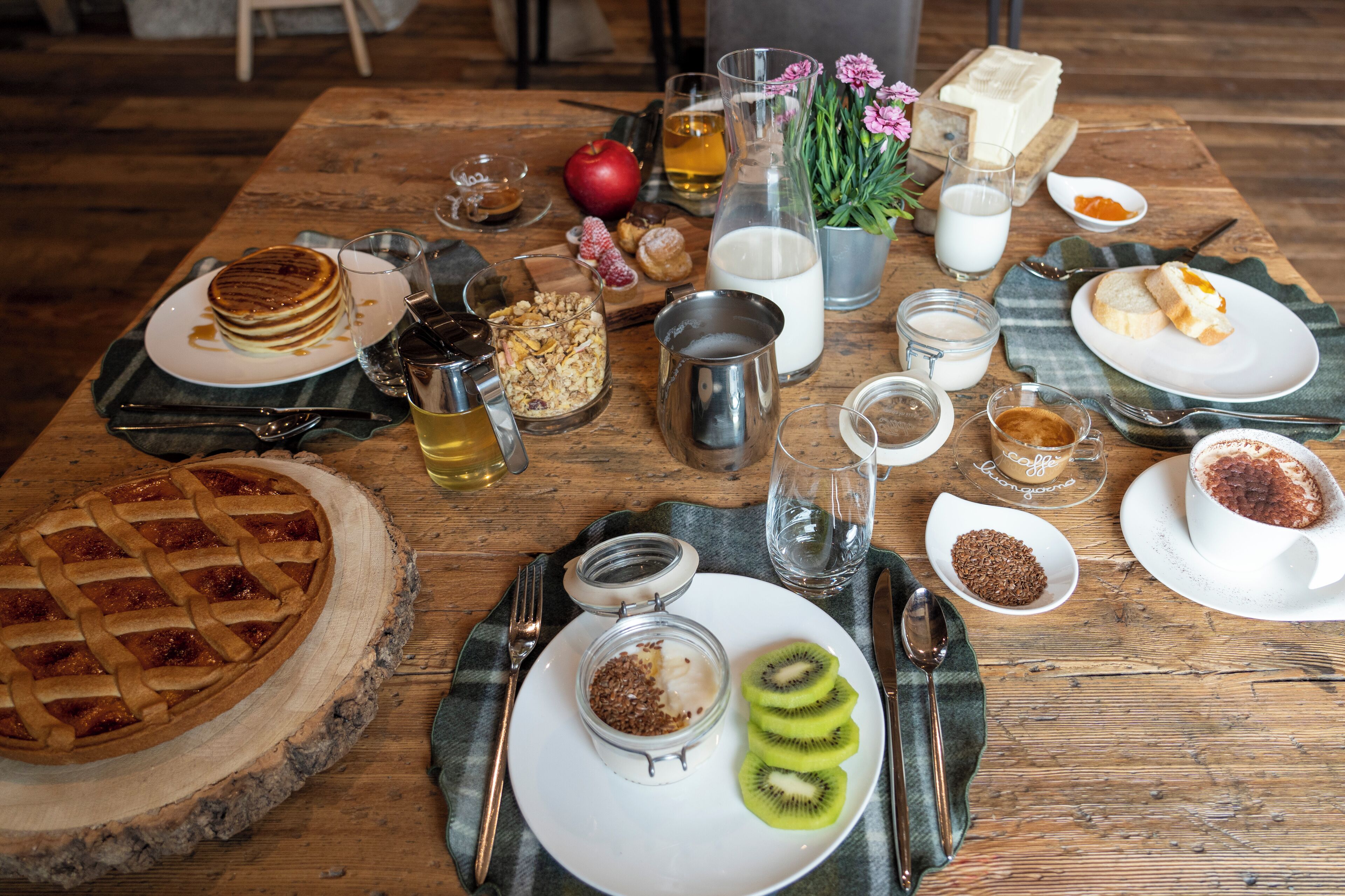 A wooden table with a variety of breakfast items including pancakes, a pie, and sliced kiwi.