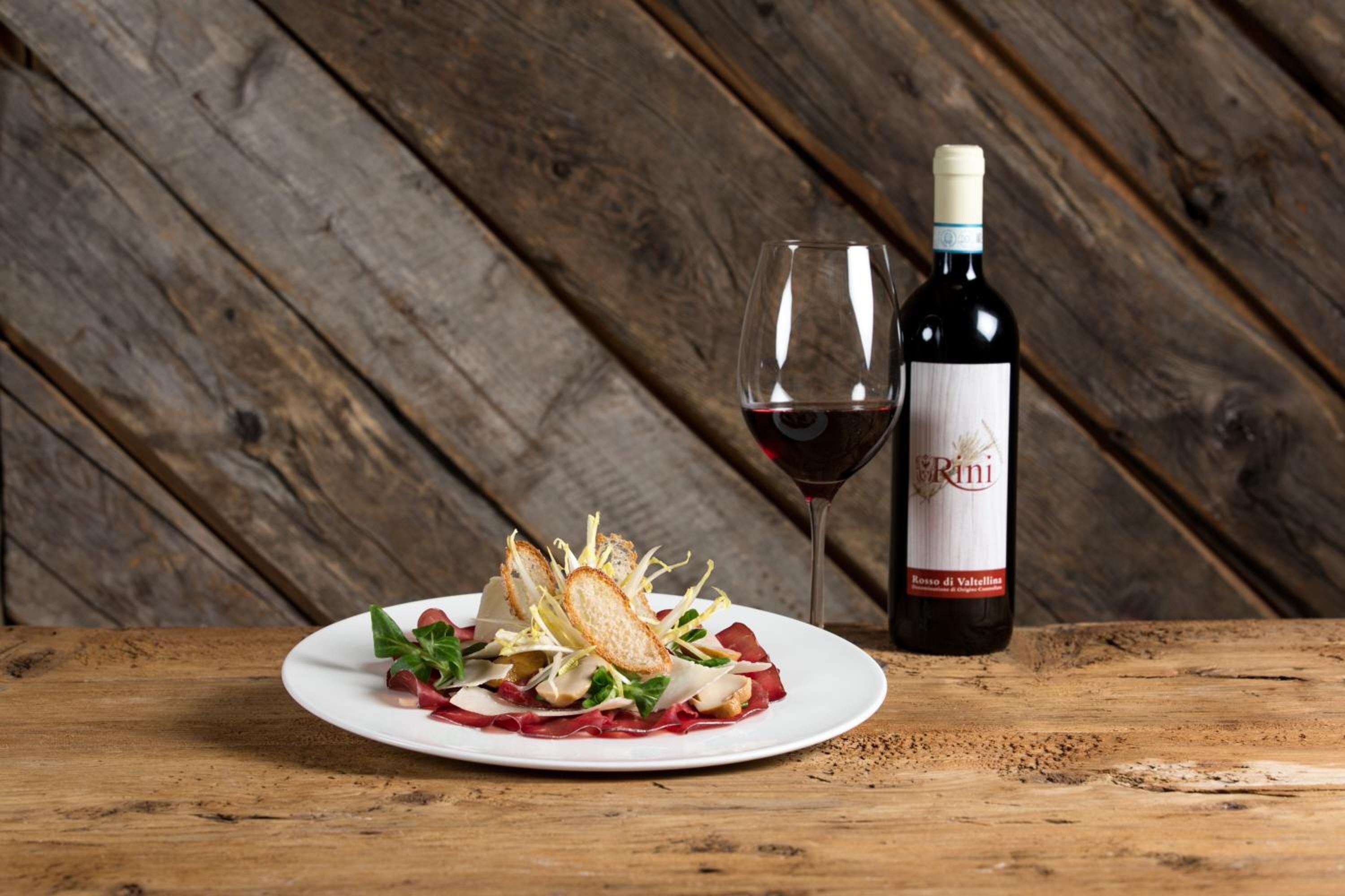 A plate of food with a bottle of wine and a glass of red wine on a wooden table.