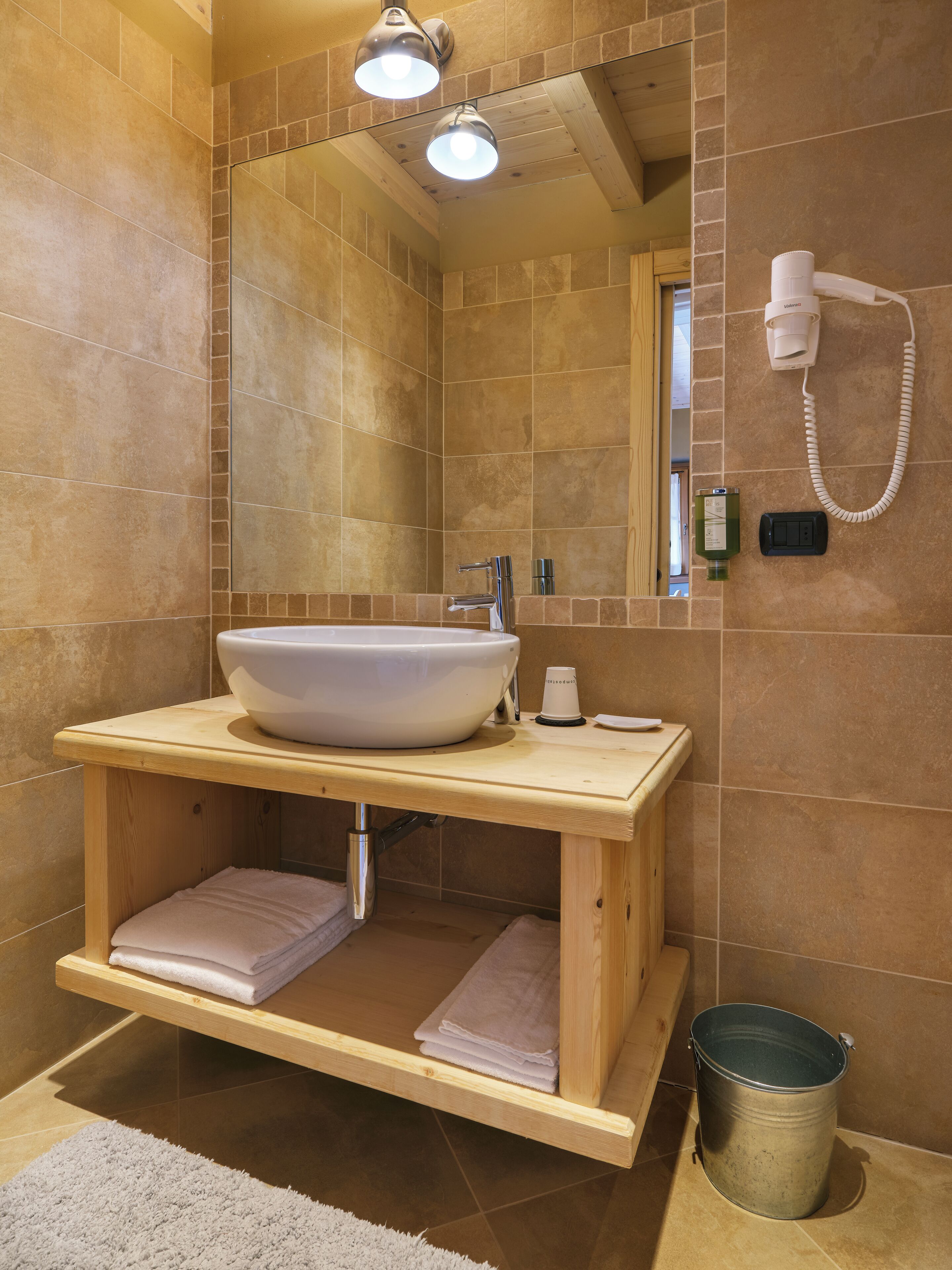 Un baño con tocador de madera, un lavamanos grande, toallero, espejo y zona de ducha.