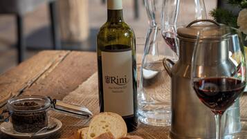 A wooden table with a bottle of wine, glasses, a pitcher, bread, and a plate of food.