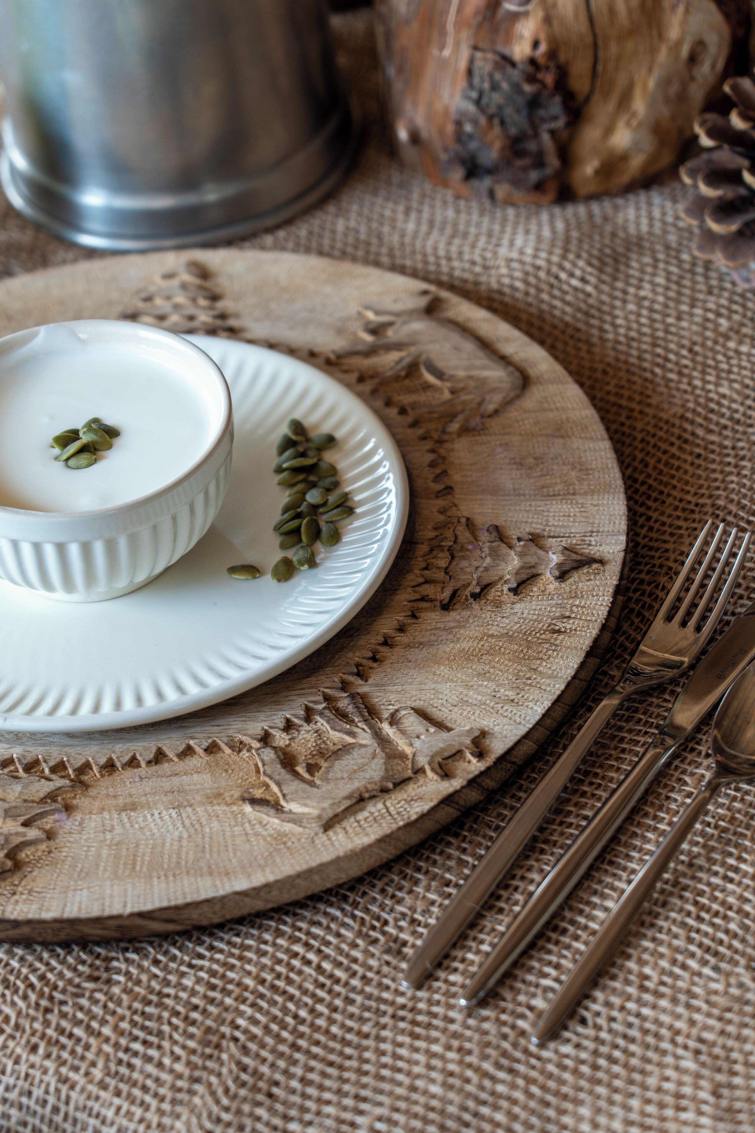 A rustic table setting with a white bowl, a plate with pumpkin seeds, and a metal pitcher.
