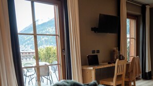 Quarto de hotel com uma cama, uma mesa com um laptop, uma cadeira e vista para montanhas pela janela.