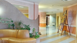 A lobby with a curved leather sofa, a planter with plants, a large column with text, and an easel with paintings. - Centrum Konferencyjno-Rekreacyjne Czarna (Czarna)