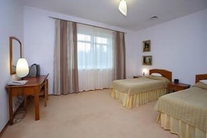 A hotel room with two beds, a desk, a chair, a lamp, and a window with curtains.