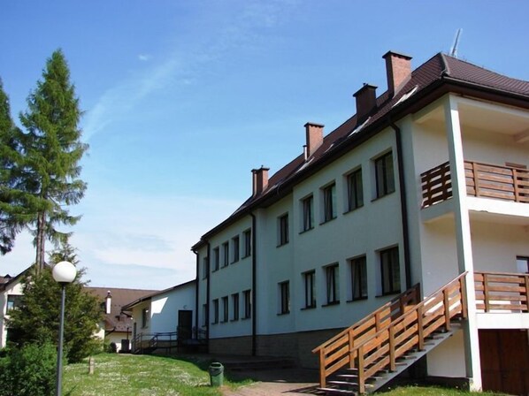 A two-story building with a white facade, multiple windows, and a wooden staircase leading to an upper level.