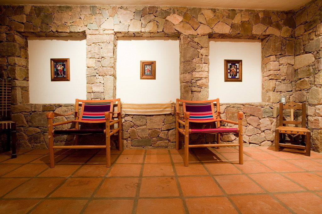 A room with stone walls, two wooden chairs with colorful cushions, and framed pictures on the walls.