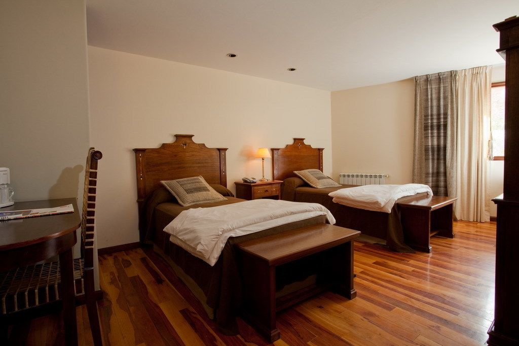 Habitación de hotel con dos camas, piso de madera, una mesita y una lámpara.