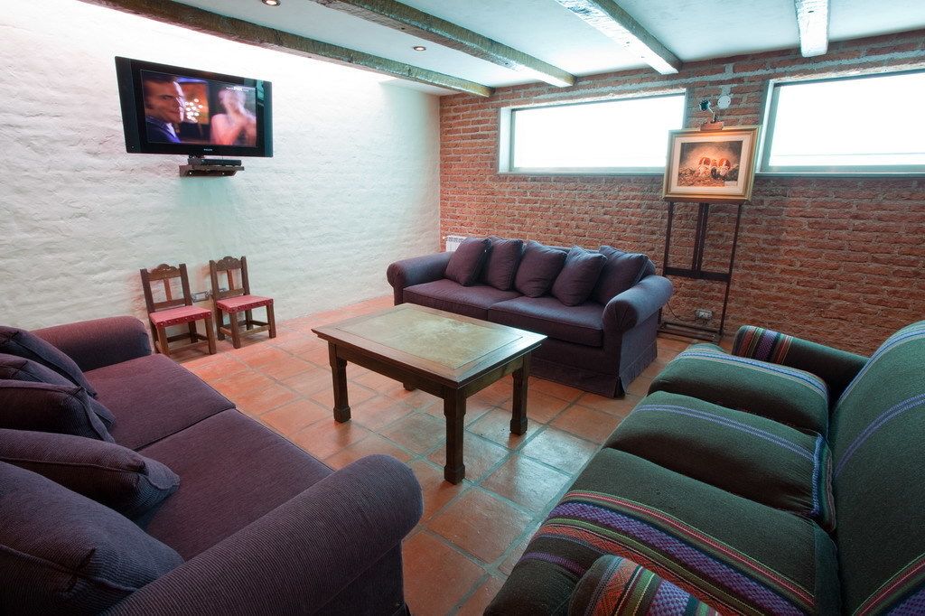 Una sala de estar con pared de ladrillo, un televisor montado en la pared, un sofá, una mesa de centro y dos sillones.