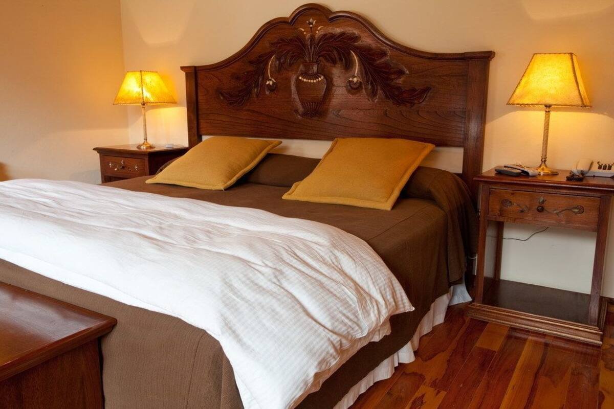 Una cama bien hecha con cabecera de madera, dos mesitas de noche con lámparas y un tocador con espejo.