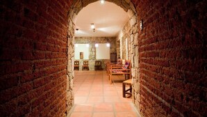 A narrow brick corridor with a stone archway leading to a room with wooden furniture and a tiled floor. - Marques de Tojo Hotel (Purmamarca)